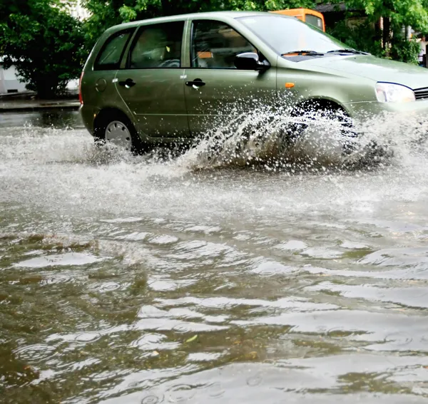 En bil kører igennem en stor mængde regnvand på en vej.